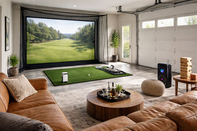 Modern garage entertainment room featuring an indoor golf simulator with turf and large screen, leather sectional, round coffee table with drinks, speaker and game-night accessories.
