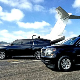 Sleek black SUVs parked beside a white private jet on a sunny airport tarmac under bright blue skies — private jet ground transport scene.