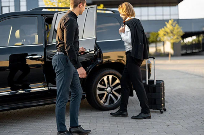 Business traveler boarding a black SUV for airport or hotel transfer while a driver opens the door; rolling suitcase on a modern urban curb