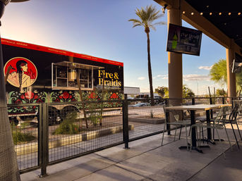 Vibrant floral-decorated food truck parked beside an outdoor patio with tables, palm trees and string lights at sunset in Scottsdale, Arizona.