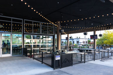 Covered urban outdoor restaurant patio with warm string lights, lounge seating, tables, glass garage doors and a sidewalk street view