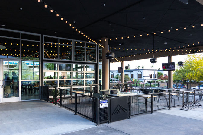 Covered urban outdoor restaurant patio with warm string lights, lounge seating, tables, glass garage doors and a sidewalk street view