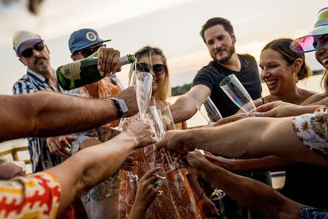 Group of friends clinking champagne flutes as champagne is poured on a boat at sunset over a lake, summer celebration on the water