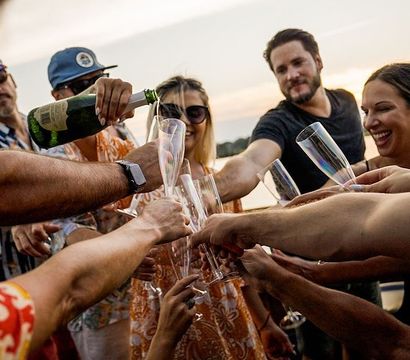 Group of friends clinking champagne flutes as champagne is poured on a boat at sunset over a lake, summer celebration on the water