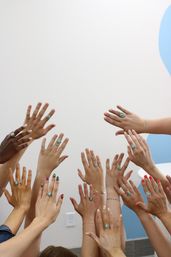 Playful cluster of diverse raised hands showing turquoise rings and colorful manicures against a white wall with a blue accent in an indoor studio