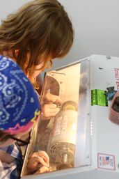 Close-up of two people polishing a small metal piece on a bench grinder inside a protective enclosure in a craft workshop.