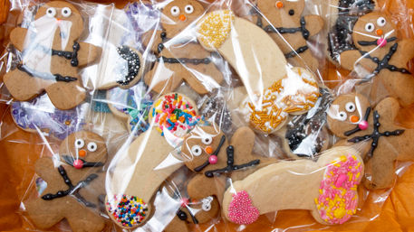 Colorful decorated gingerbread men and novelty frosted cookies with sprinkles, individually wrapped in clear bags and arranged in an orange gift box as festive party favors.