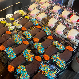 Rows of homemade horseshoe-shaped cookies cooling on a rack — chocolate and vanilla varieties topped with colorful sprinkles and nonpareils in orange, blue, pink and yellow.