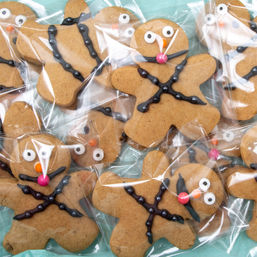 Pile of individually wrapped gingerbread people cookies decorated with chocolate icing X-patterns and candy eyes on a teal background, festive holiday treat