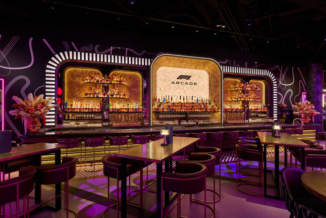 Neon-lit arcade-inspired bar interior with illuminated liquor shelves, marble feature wall, high tables and velvet stools, purple and gold ambient lighting creating a modern nightlife lounge atmosphere