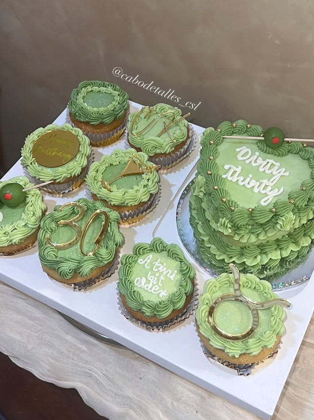 Mint-green buttercream cupcakes and matching mini layered cake on a white board — martini-themed 30th birthday desserts with gold accents, olive picks, piped “Dirty Thirty” and “A tini bit older” lettering.