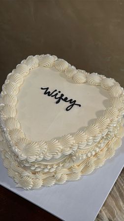Heart-shaped vanilla buttercream celebration cake with ruffled piped border and 'wifey' written in black script