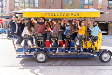 Group of friends toasting with drinks on a yellow mobile trolley bar rolling along a sunny downtown city street