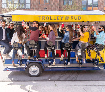 Group of friends toasting with drinks on a yellow mobile trolley bar rolling along a sunny downtown city street