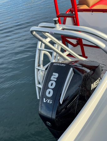 Black Mercury 200 V6 outboard mounted on a pontoon stern with curved silver aluminum rails and a red boarding ladder above calm lake water.