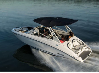 White recreational speedboat cruising on calm water with three passengers relaxing under a black canopy, leaving a foamy wake behind.