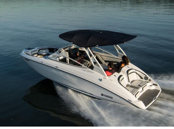 White recreational speedboat cruising on calm water with three passengers relaxing under a black canopy, leaving a foamy wake behind.