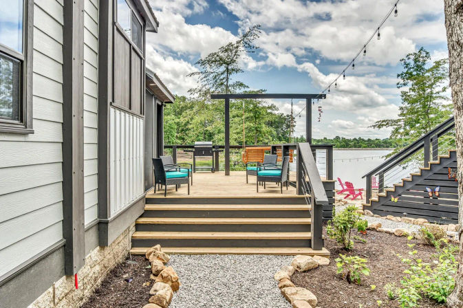 Lakefront wooden deck with turquoise-cushioned chairs, grill, string lights, stairs and shoreline view