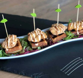Skewered bite-sized chicken-and-waffle appetizers — crispy fried chicken atop mini waffles, drizzled with sauce and served on a bed of mixed greens