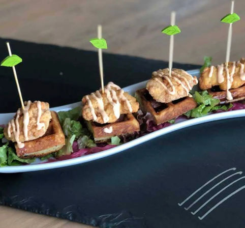 Skewered bite-sized chicken-and-waffle appetizers — crispy fried chicken atop mini waffles, drizzled with sauce and served on a bed of mixed greens