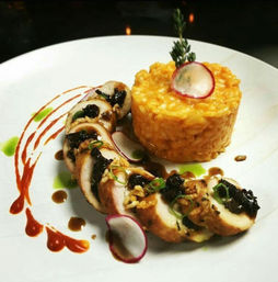 Gourmet plated entrée of sliced stuffed chicken roulade with crunchy topping, paired with a creamy yellow risotto tower, garnished with radish slices, herb sprig and artistic red and green sauce swirls on a white plate