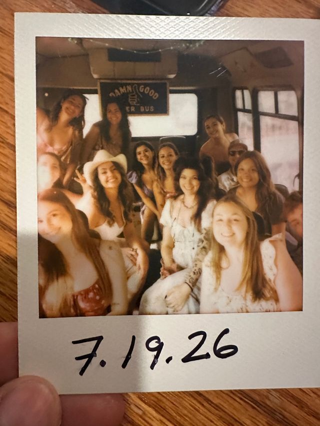 Polaroid snapshot of a smiling group of friends on a party bus, warm vintage tones, summer outfits and a cowboy hat, handwritten date “7.19.26” at the bottom.