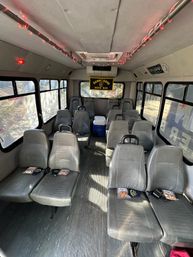 Interior of a converted shuttle/party bus with gray vinyl seats in rows, red LED ceiling lights, a yellow beer banner at the rear and a cooler in the aisle.