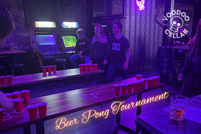 Purple-lit bar interior hosting a beer pong tournament: wooden tables lined with red cups, players mid-throw, neon skull sign and retro arcade machines in the background.