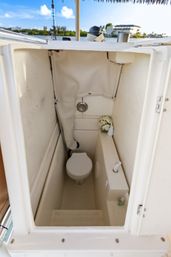 Cozy compact marine head on a boat: white toilet, small sink/faucet, decorative flowers and a waterfront view.