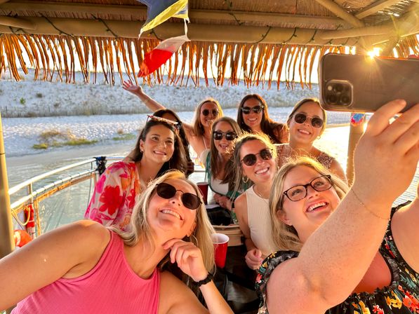 Group of friends taking a selfie on a tiki-roof boat by a sandy beach at sunset, sunglasses and golden-hour, festive coastal vibe