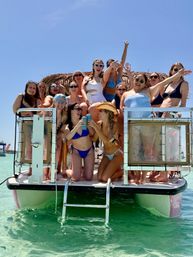 Sunlit pontoon boat party with a group of women in swimsuits cheering and clinking drinks over clear turquoise water for tropical beach vibes