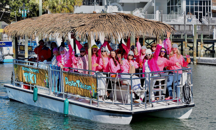 Cheerful group in pink hoodies on a tiki-style pontoon boat cruising a sunny coastal marina