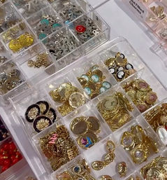 Clear plastic organizer tray of gold-tone charms, cameo pendants, decorative buttons and metal findings — jewelry supplies at a craft market or bead shop display.