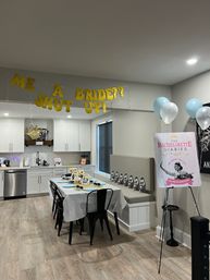 Modern kitchen and dining area set up for a bachelorette party with gold glitter banner, decorated table with photo props and blue-and-white balloons