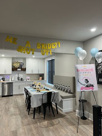 Modern kitchen and dining area set up for a bachelorette party with gold glitter banner, decorated table with photo props and blue-and-white balloons