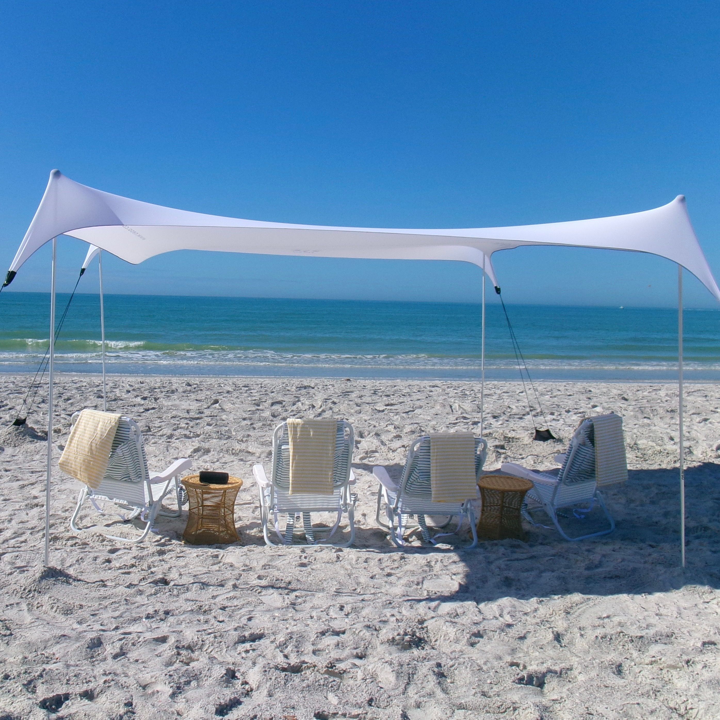 White stretch canopy and striped lounge chairs on a sandy beach facing turquoise ocean under a clear blue sky