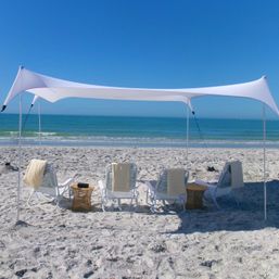White stretch canopy and striped lounge chairs on a sandy beach facing turquoise ocean under a clear blue sky