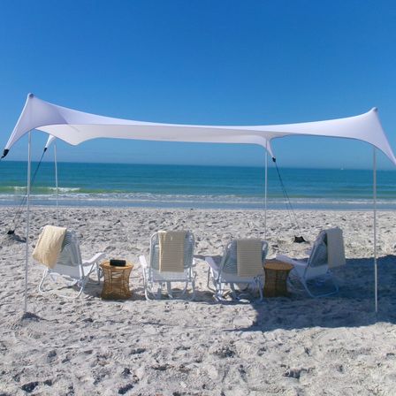 White stretch canopy and striped lounge chairs on a sandy beach facing turquoise ocean under a clear blue sky