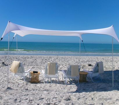 White stretch canopy and striped lounge chairs on a sandy beach facing turquoise ocean under a clear blue sky