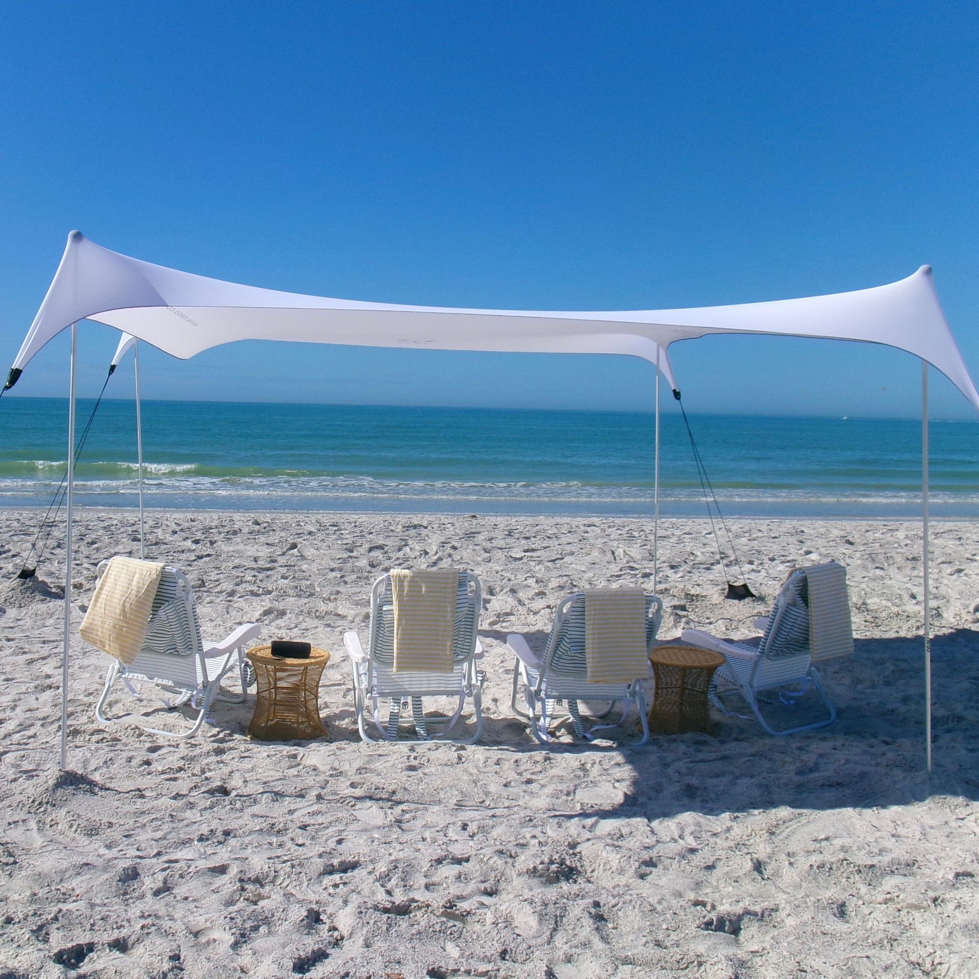 White stretch canopy and striped lounge chairs on a sandy beach facing turquoise ocean under a clear blue sky