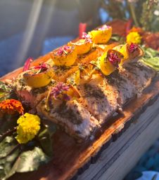 Planked grilled salmon fillets topped with roasted lemon halves, fresh dill and edible flower petals on a rustic wooden serving board, styled for outdoor dining.