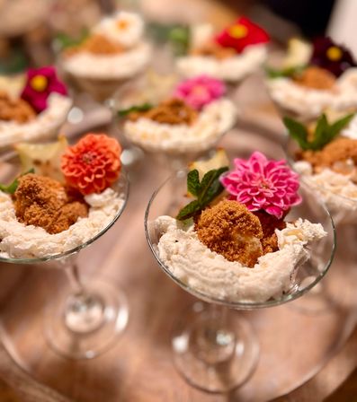 Mini dessert parfaits in martini glasses with whipped cream, crunchy crumb-topped bites, bright edible flowers and mint garnish
