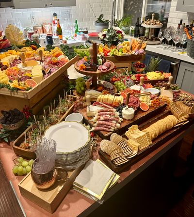 Vibrant charcuterie grazing spread on a home kitchen island with cheeses, cured meats, crackers, fresh fruit, veggies, dips, skewers and wine