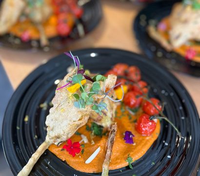 Colorful gourmet appetizer: crispy battered vegetable skewer on a black plate with roasted cherry tomatoes, vibrant red pepper purée, microgreens and edible flowers — restaurant plating.