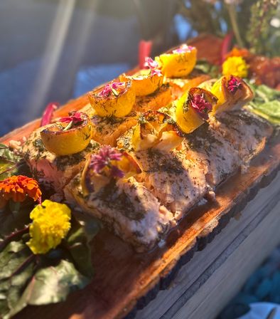Plank-roasted salmon fillets topped with grilled lemon halves, fresh dill and vibrant edible flowers on a rustic wooden serving board