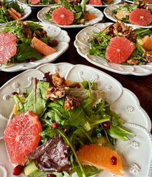 Bright citrus salad with grapefruit and orange segments, mixed baby greens, pomegranate seeds and candied walnuts on white ceramic plates arranged on a wooden table.