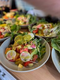 Close-up of vibrant fresh salad bowls on a wooden counter with mixed greens, sliced radishes, cherry tomatoes, cucumber rounds, microgreens and a glossy vinaigrette