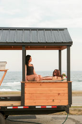 Two women relaxing in a wooden beachfront cabana with an ocean view — seaside summer scene, sunglasses and coastal vibes.