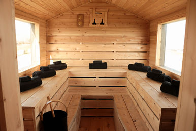 Cozy cedar sauna cabin interior with tiered wooden benches, black rolled towels, bucket and bright side windows