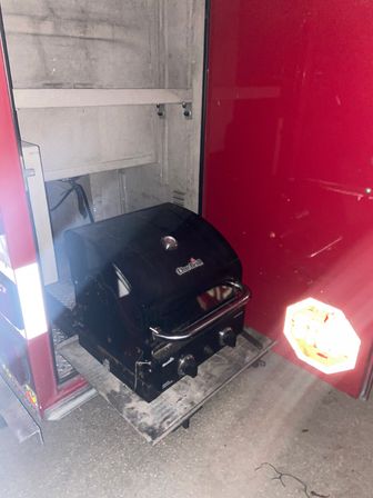 Black Char-Broil portable gas grill on a slide-out shelf inside a red RV storage compartment, camping-ready.